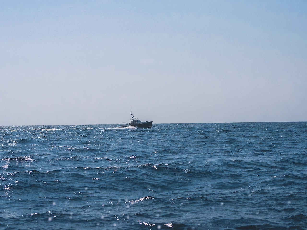 Lone fishing boat sails on a vast ocean under a clear sky, showcasing maritime tranquility.